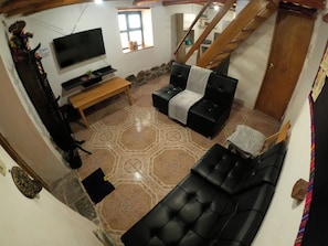 A living room with a black sofa, a wooden bench, and a TV mounted on the wall. - SUMAQ WASI (Cusco)
