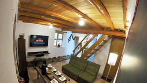 Ein gemütliches Wohnzimmer mit einem grünen Sofa, Holzboden, Kamin und einem an der Wand befestigten Fernseher.