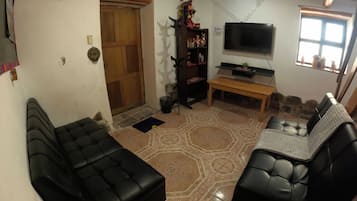Un salon avec deux canapés en cuir noir, un banc en bois, un téléviseur et une porte.