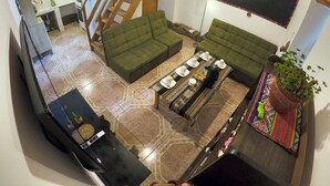 Ein großzügiger Wohnbereich mit einem grünen Sofa, einem Couchtisch und einem Esstisch, gedeckt für vier Personen. Eine Treppe führt auf eine obere Ebene.
