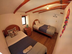 A bedroom with two beds, wooden beams on the ceiling, a window with curtains, and a wall with a hanger.