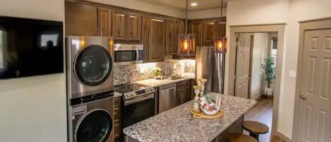 A kitchen with stainless steel appliances, wooden cabinets, and a granite island with bar stools.