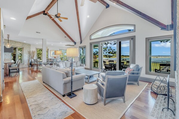 A spacious living room with a high ceiling, large windows, and a view of the outdoors.