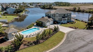 A residential area with a large house featuring a swimming pool, dock, and a view of a river. - Summer Baycation | Waterfront | Private Pool, Hot Tub (Virginia Beach)