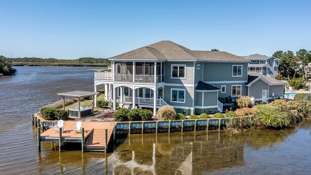 A two-story waterfront house with a dock, outdoor seating, and a covered patio. - Summer Baycation | Waterfront | Private Pool, Hot Tub (Virginia Beach)