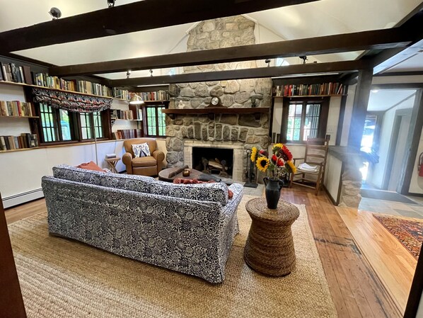A cozy living room with a patterned sofa, a fireplace, and bookshelves filled with books. - Charming Cottage in the Heart of the Shawangunks (Wallkill)