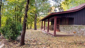 A rustic cabin with a stone foundation and a wooden porch, surrounded by dense forest and autumn foliage. - Charming Cottage in the Heart of the Shawangunks (Wallkill)