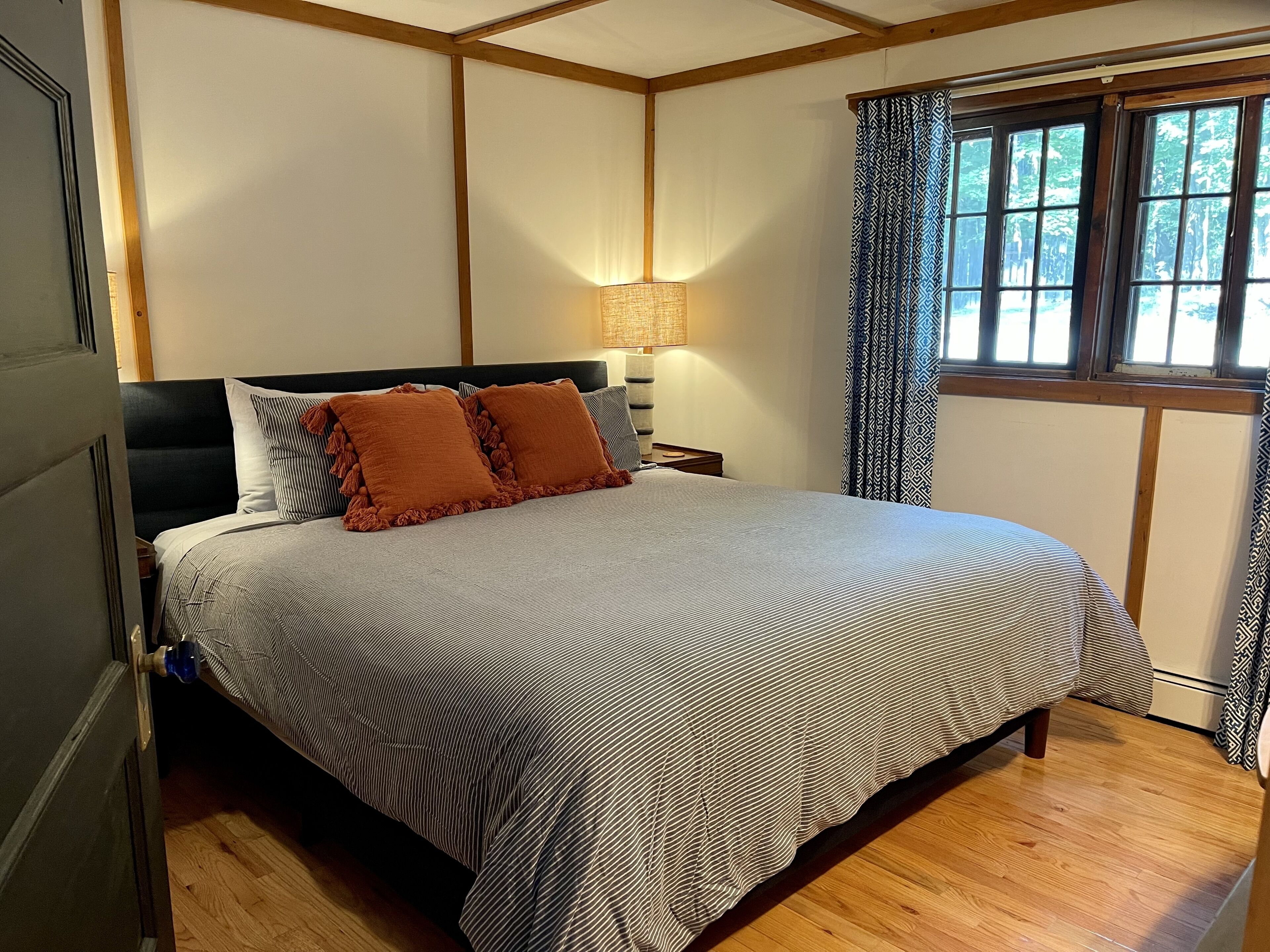 A neatly made bed with striped bedding, a bedside lamp, and a window with patterned curtains.