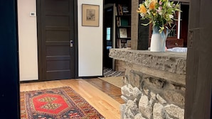 A hallway with a patterned rug, a stone wall, a vase with flowers, and a door with a framed picture. - Charming Cottage in the Heart of the Shawangunks (Wallkill)