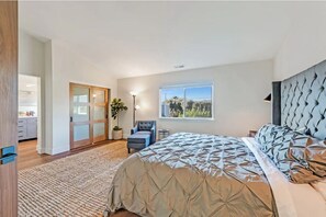 Quarto com uma cama grande, escrivaninha, cadeira, janela com vista e porta de correr para um banheiro.