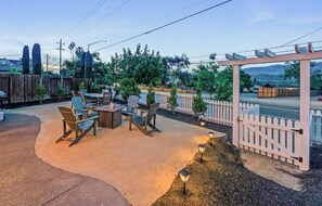 Uma área de estar ao ar livre com pergolado, assentos e vista para a rua.