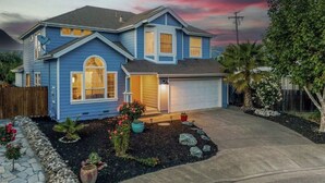 A two-story house with a garage, a driveway, and a landscaped front yard with various plants and a small rock garden. - Updated 5 BR house w/ hot tub - 5 min walk to downtown! (Geyserville)