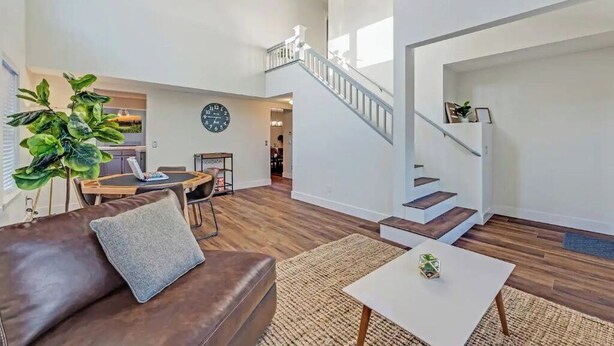 A spacious living area with a brown leather sofa, a white coffee table, and a large green plant. A staircase with white railings leads to an upper level. - Updated 5 BR house w/ hot tub - 5 min walk to downtown! (Geyserville)