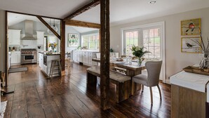 Una cocina amplia con pisos de madera, una zona de comedor con banco y vistas al jardín a través de grandes ventanales.