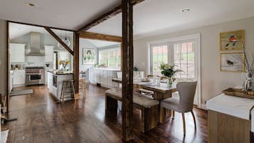 A spacious kitchen with wooden floors, a dining area with a bench, and a view of the garden through large windows.