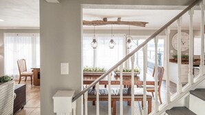 A staircase with a rustic wooden beam ceiling, a dining area with a wooden table and chairs, and hanging pendant lights.