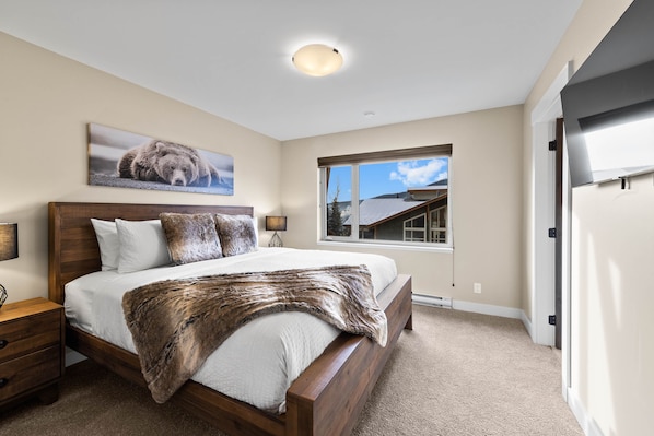 Relax in this serene bedroom with a large bed, framed artwork, and a window offering a city view.
