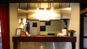 Una recepción con encimera de madera y base de acero inoxidable, iluminación colgante y una cortina roja a la izquierda.