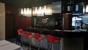 A bar area with a counter, red bar stools, hanging pendant lights, and a refrigerator with a Red Bull logo.