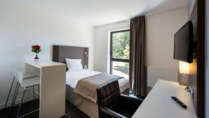 Ein Hotelzimmer mit Bett, Schreibtisch, Stuhl, Fernseher und einem Fenster mit Vorhängen.