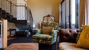 Een woonkamer met een trap, een gestreept fauteuil, een leren bank en een groot raam met gordijnen.