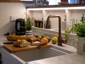 A kitchen with a wooden cutting board, various fruits, cheese, and a bread loaf. - John Campbell Apartment (Dunedin)