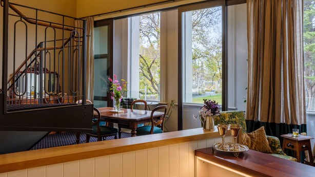 Een eetruimte met een houten tafel en stoelen, een piano en uitzicht op het omliggende landschap door grote ramen.