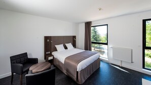 A modern hotel room with a large bed, a desk, a chair, and a window with a view of greenery. - Séjour Moderne 100m du Centre|Wi-Fi+Parking Inclus (Dijon)