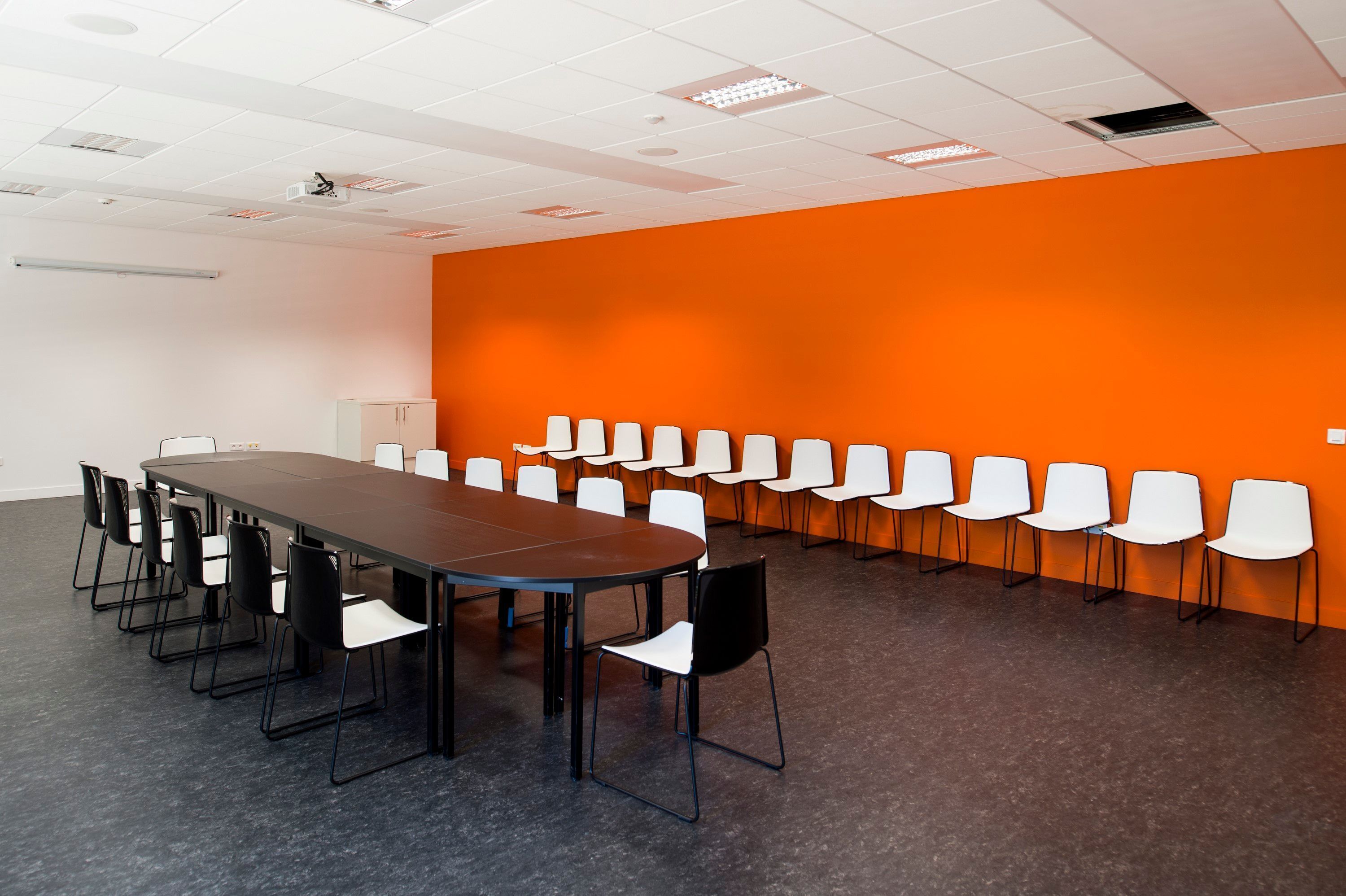 A conference room with a long table and chairs, white walls, and an orange accent wall.