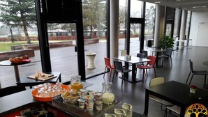 A breakfast setup with various food items and beverages on a table, large windows offering a view of the outdoors, and a modern interior design. - Séjour Moderne 100m du Centre|Wi-Fi+Parking Inclus (Dijon)