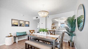 Un comedor con una mesa de madera, banco y sillas, una araña y plantas en macetas.