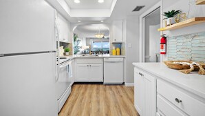 Una cocina moderna con armarios blancos, piso de madera y vista al comedor.
