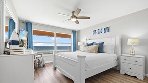 Un dormitorio con cama, mesitas de noche, ventilador de techo, ventana con vistas y cómoda.