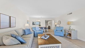 A modern living room with a sofa, two armchairs, a coffee table, and a dining area with a chandelier. - Cape Canaveral Condo W/ Direct Ocean Views, Steps to Beach, & Pool Access! ☀️ (Cape Canaveral)