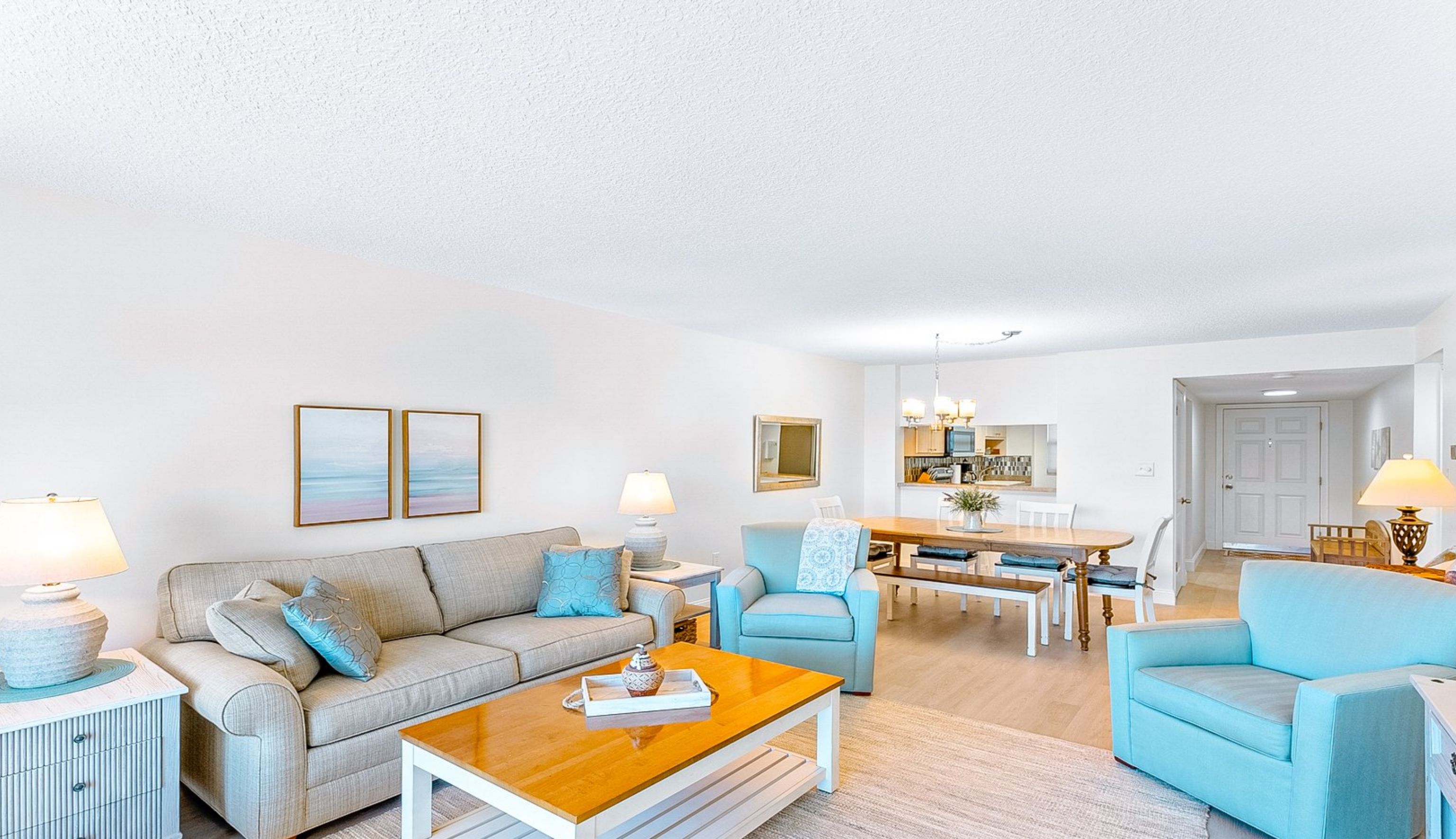 A living room with a sofa, armchair, and coffee table. There is a dining area in the background.