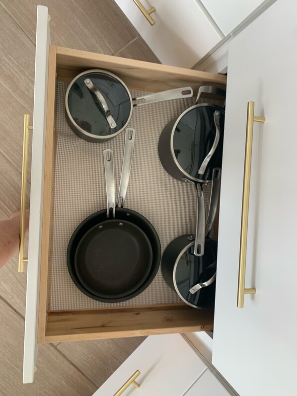 Un tiroir de cuisine contenant un tapis, trois poêles et deux spatules.