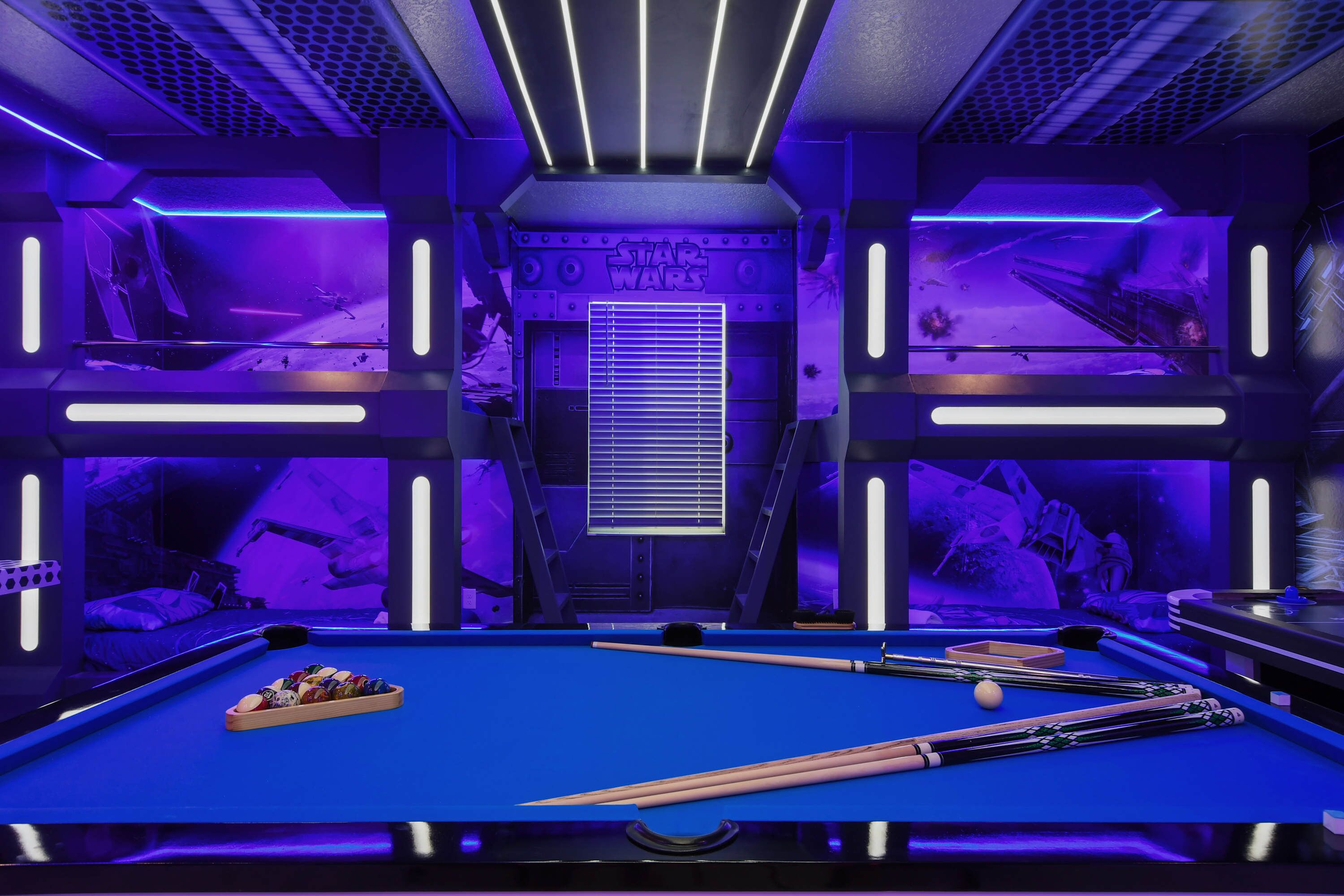 Ein Billardtisch mit einem Star Wars Hintergrund, einer blauen Spielfläche und Billardstöcken.