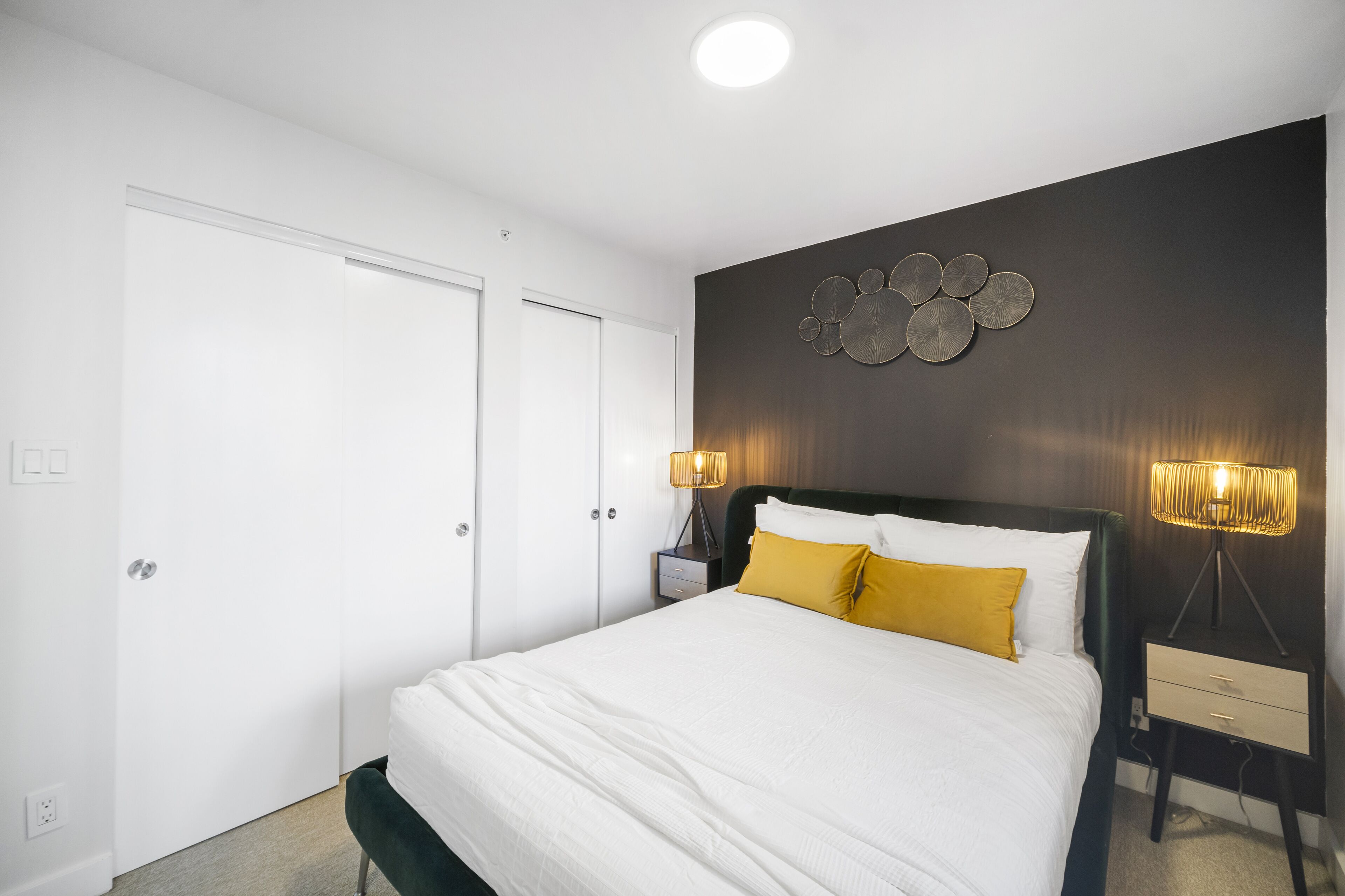 Quarto com cama, mesa de cabeceira com abajur, obra de arte na parede e porta.