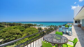 A balcony with a view of the ocean and beach, green chairs, and a table.
