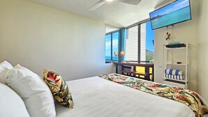 A hotel room with a bed, a desk with a computer, a TV, and a view of the ocean.