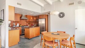 A modern kitchen with wooden cabinets, a central island, and a dining area with a round table and chairs. - Unique 2 Master Suite Pool/ Spa Home, Relaxing Yard with Mountain Views (Palm Springs)