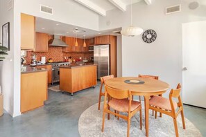 A modern kitchen with wooden cabinets, a central island, and a dining area with a round table and chairs. - Unique 2 Master Suite Pool/ Spa Home, Relaxing Yard with Mountain Views (Palm Springs)