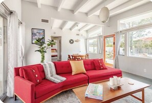 A living room with a red sofa, a coffee table with a board game, and large windows. - Unique 2 Master Suite Pool/ Spa Home, Relaxing Yard with Mountain Views (Palm Springs)