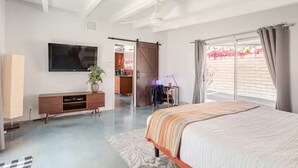 A bedroom with a bed, a TV, a sliding door to a balcony, and a desk with a chair. - Unique 2 Master Suite Pool/ Spa Home, Relaxing Yard with Mountain Views (Palm Springs)