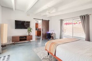 A bedroom with a bed, a TV, a sliding door to a balcony, and a desk with a chair. - Unique 2 Master Suite Pool/ Spa Home, Relaxing Yard with Mountain Views (Palm Springs)