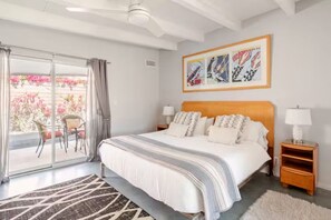 A bedroom with a bed, a nightstand, a lamp, a ceiling fan, a sliding glass door, and a balcony with chairs. - Unique 2 Master Suite Pool/ Spa Home, Relaxing Yard with Mountain Views (Palm Springs)