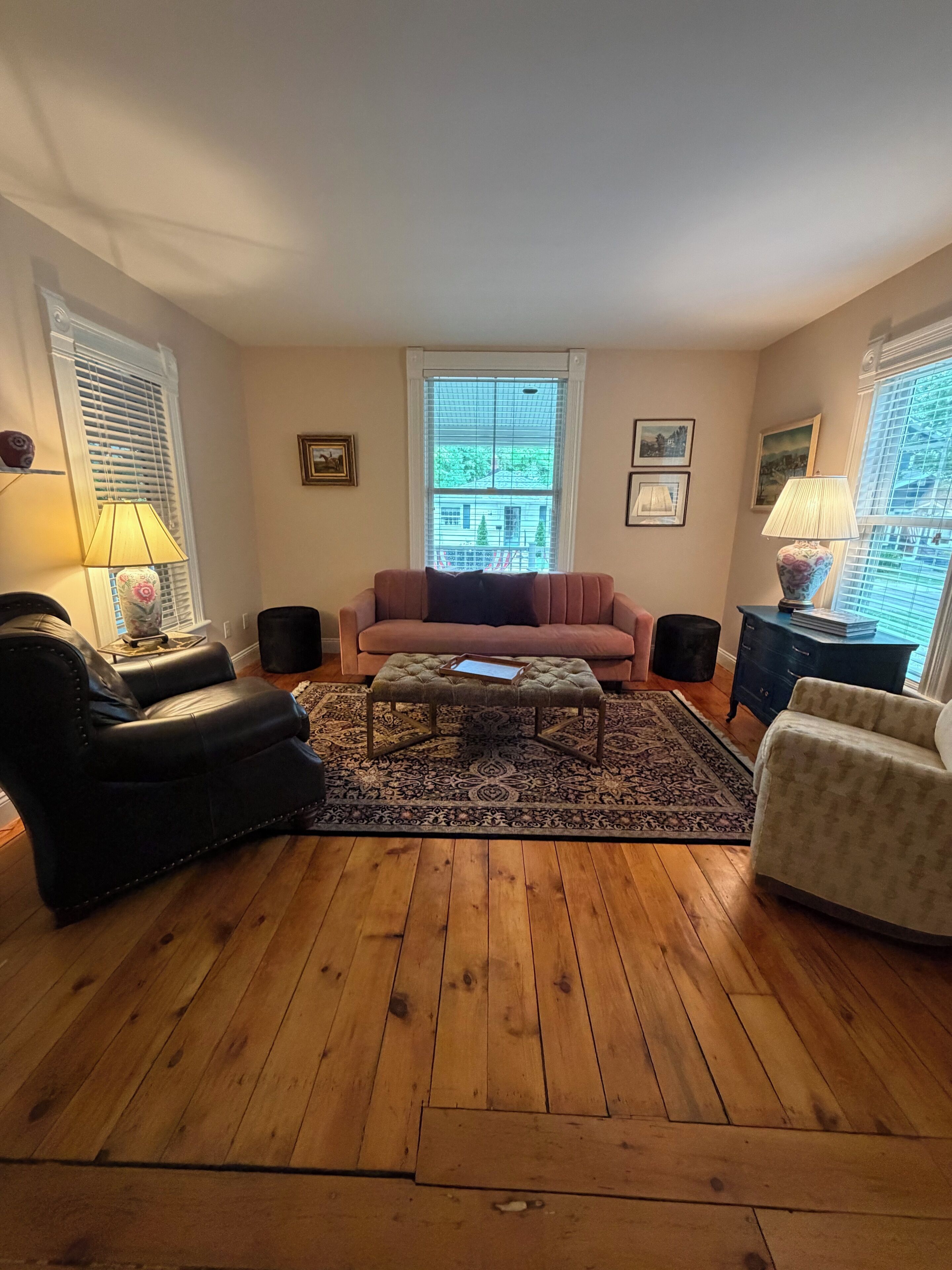 Una sala de estar con piso de madera, un sofá, un sillón, una mesa de centro y dos lámparas.