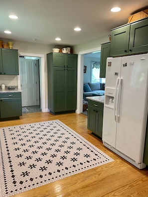 A kitchen with green cabinets, a white refrigerator, and a patterned rug on the floor.