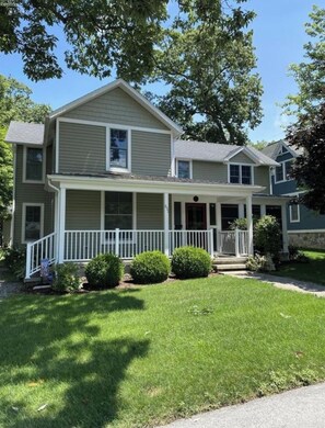 A two-story house with a front porch, a covered entryway, and a small front yard with trimmed bushes.