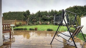 Eine Holzterrasse mit Schaukelstuhl und Tisch, umgeben von einem Garten mit Hecke und Holzzaun.
